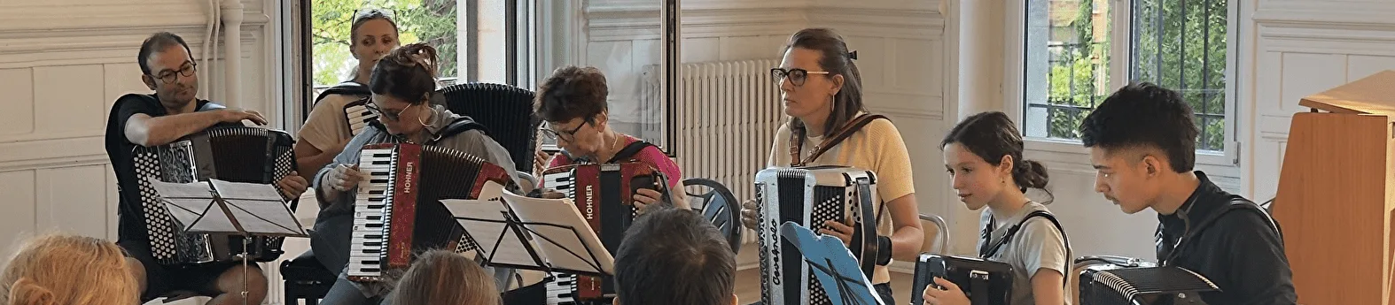 Des élèves, partitions sur pupitre, jouent ensemble de l’accordéon dans une salle lumineuse.