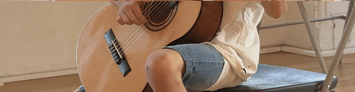 Un jeune élève assis joue de la guitare classique.