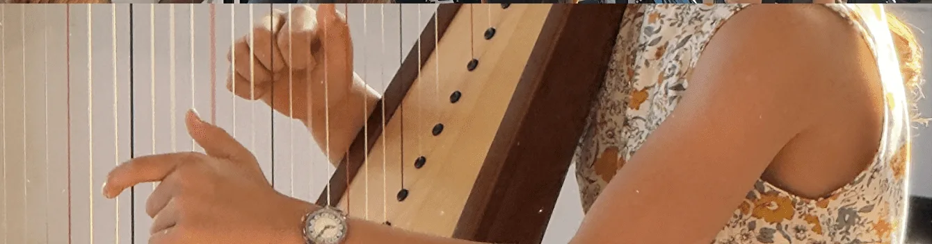 Gros plan sur les mains d’une élève pinçant les cordes d’une harpe.